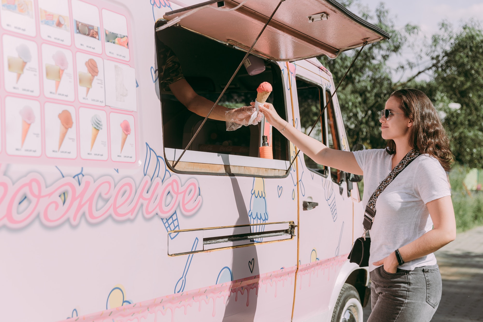 a girl buys ice cream in a pink ice cream van in a Park in summer