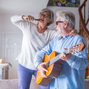 Couple of two happy seniors or mature and old people singing and dancing together at home