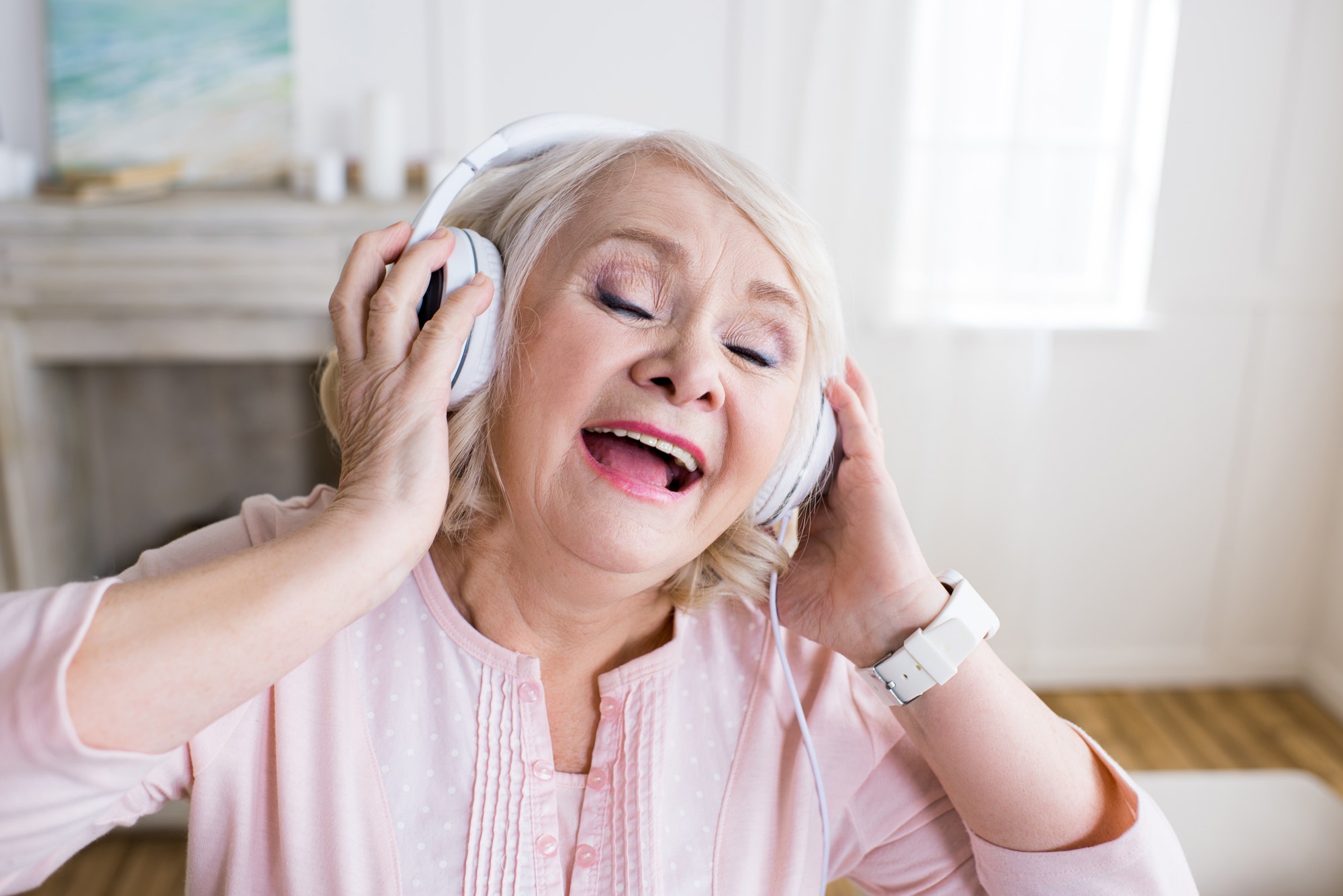 Happy senior woman with closed eyes wearing headphones and singing
