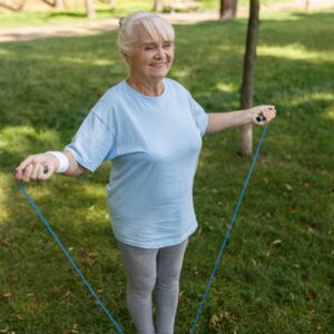 Happy senior woman in sportswear does excercise with jump rope in green park