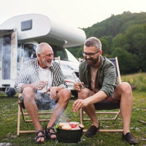Mature man with senior father talking at campsite outdoors, barbecue on caravan holiday trip