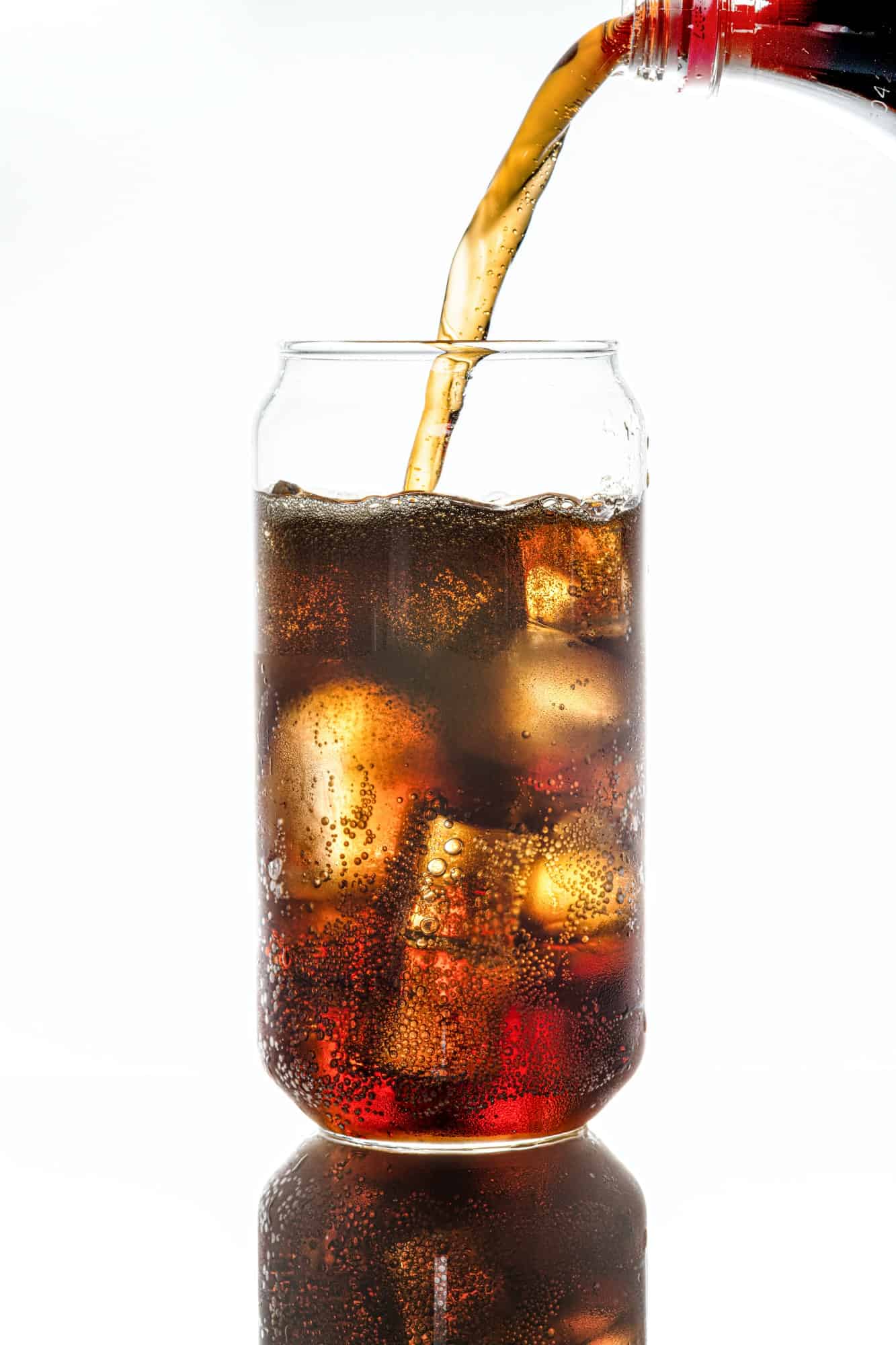 Cold carbonated drink being poured over ice cubes in a can shaped glass