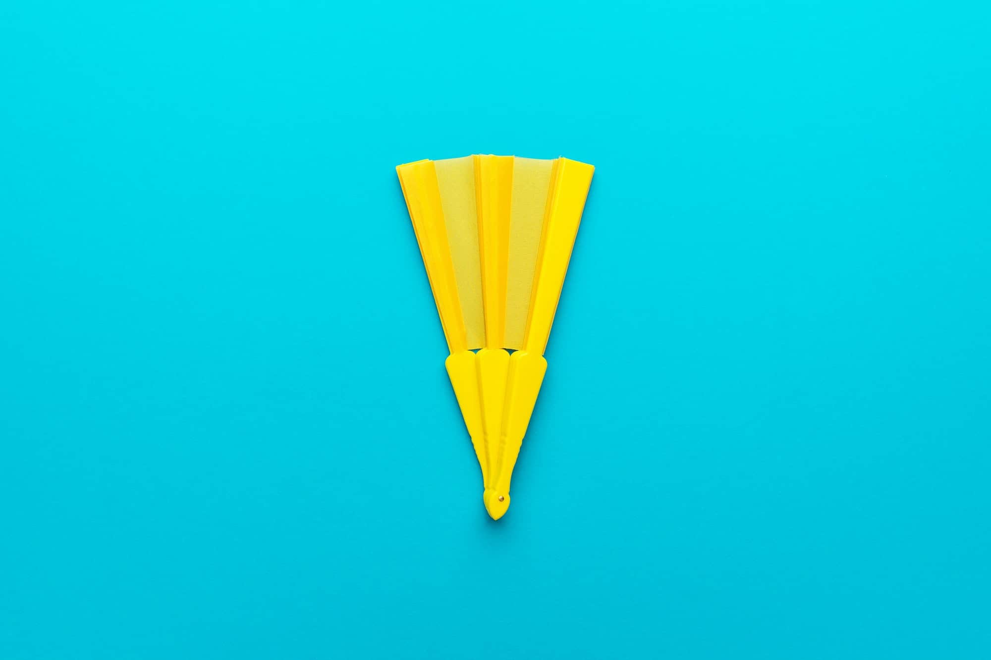 Minimalist Photo Of Yellow Hand Fan On Turquoise Blue Background With Copy Space