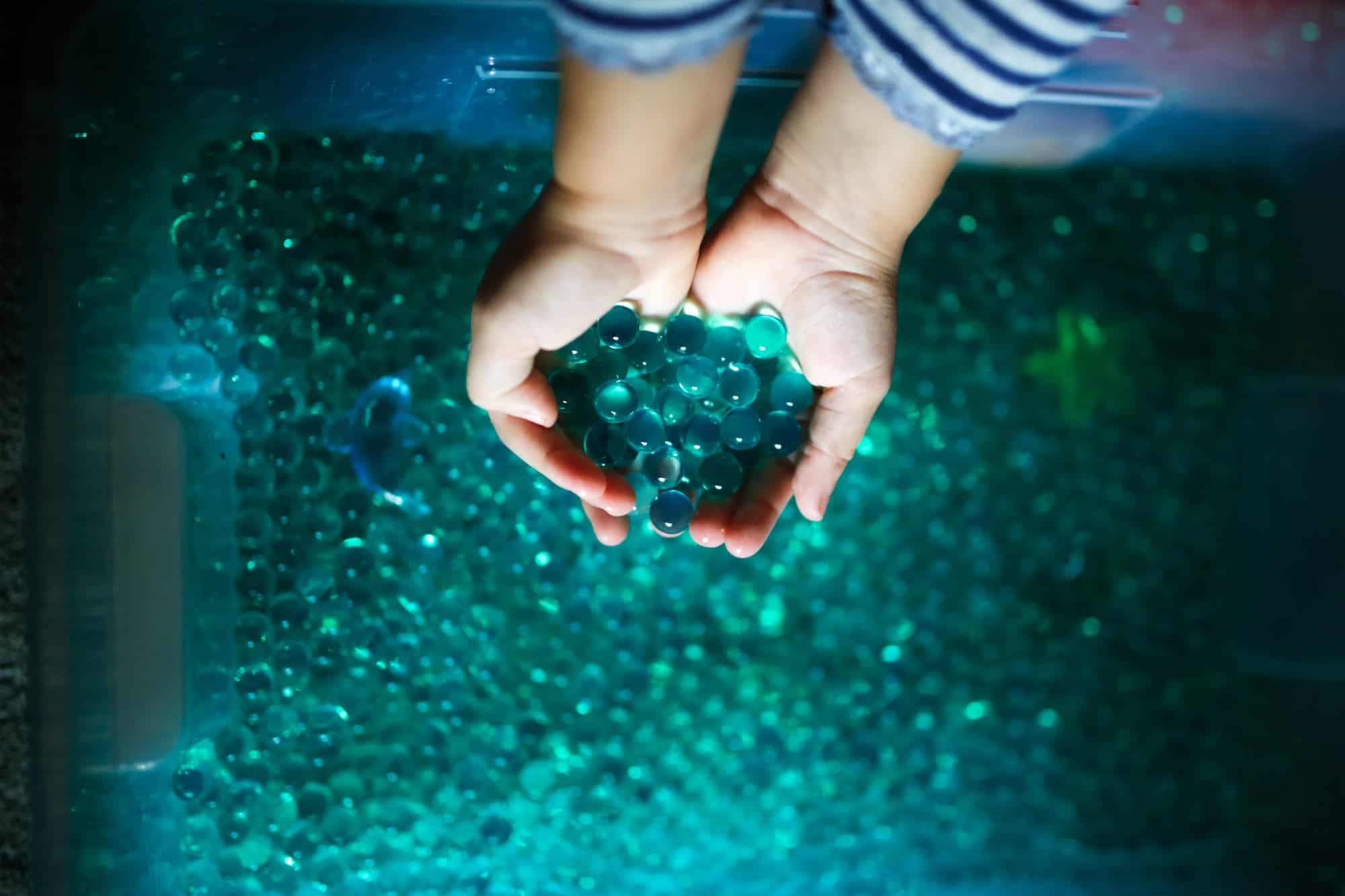 Child plays with hydrogel sensory box, children's hands touch play with blue water beads