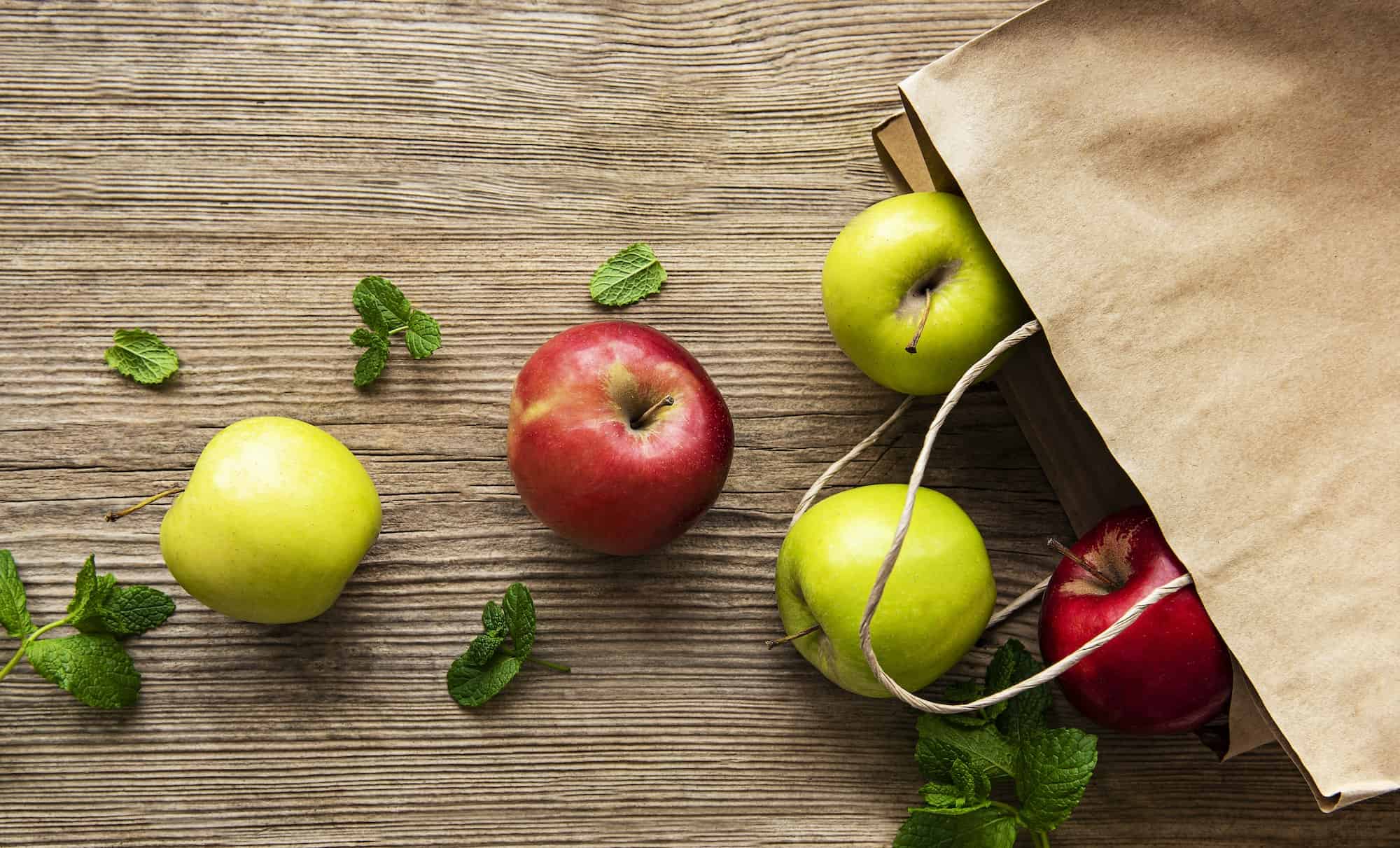 Fresh apples in a paper bag on a wooden background