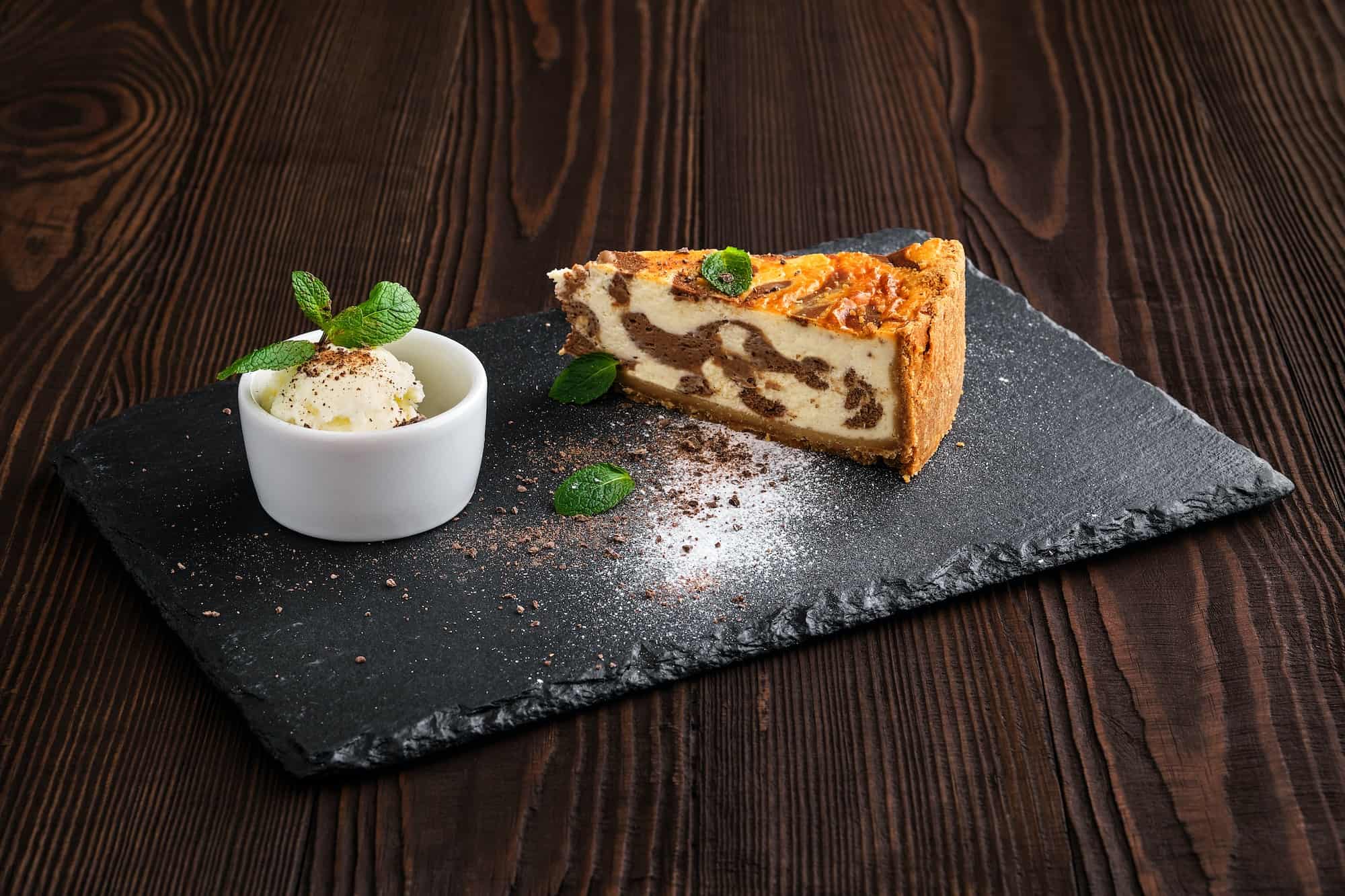 Layered cheesecake with ice cream served on slate plate