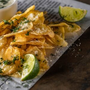 Potato Chips With Salt Near Sliced Lime, Garlic Sauce And Newspaper on Marble Surface
