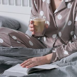 Woman sitting on bed holding cup with hot beverage in hands. Harmony, love youself wellbeing concept