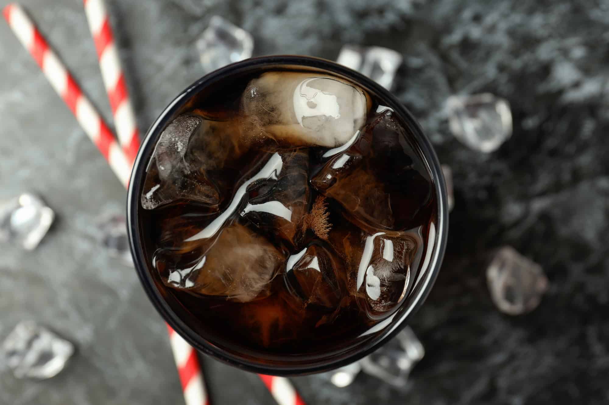 Glass of cola, ice and straws on black smokey background